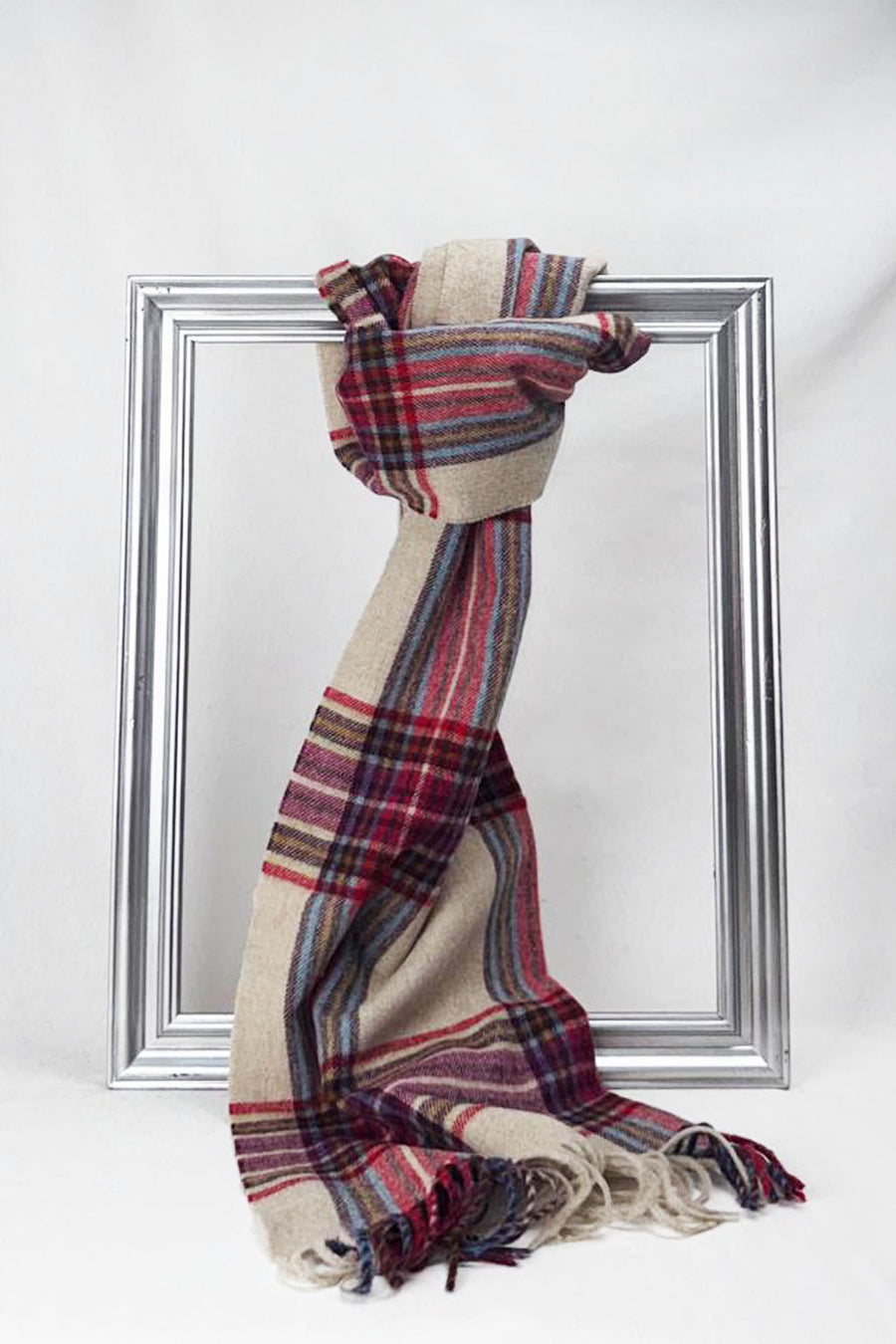 Luxurious merino wool scarf in beige with bold red and blue check patterns, draped beautifully over a silver frame. A soft and elegant unisex accessory for winter in Malta.