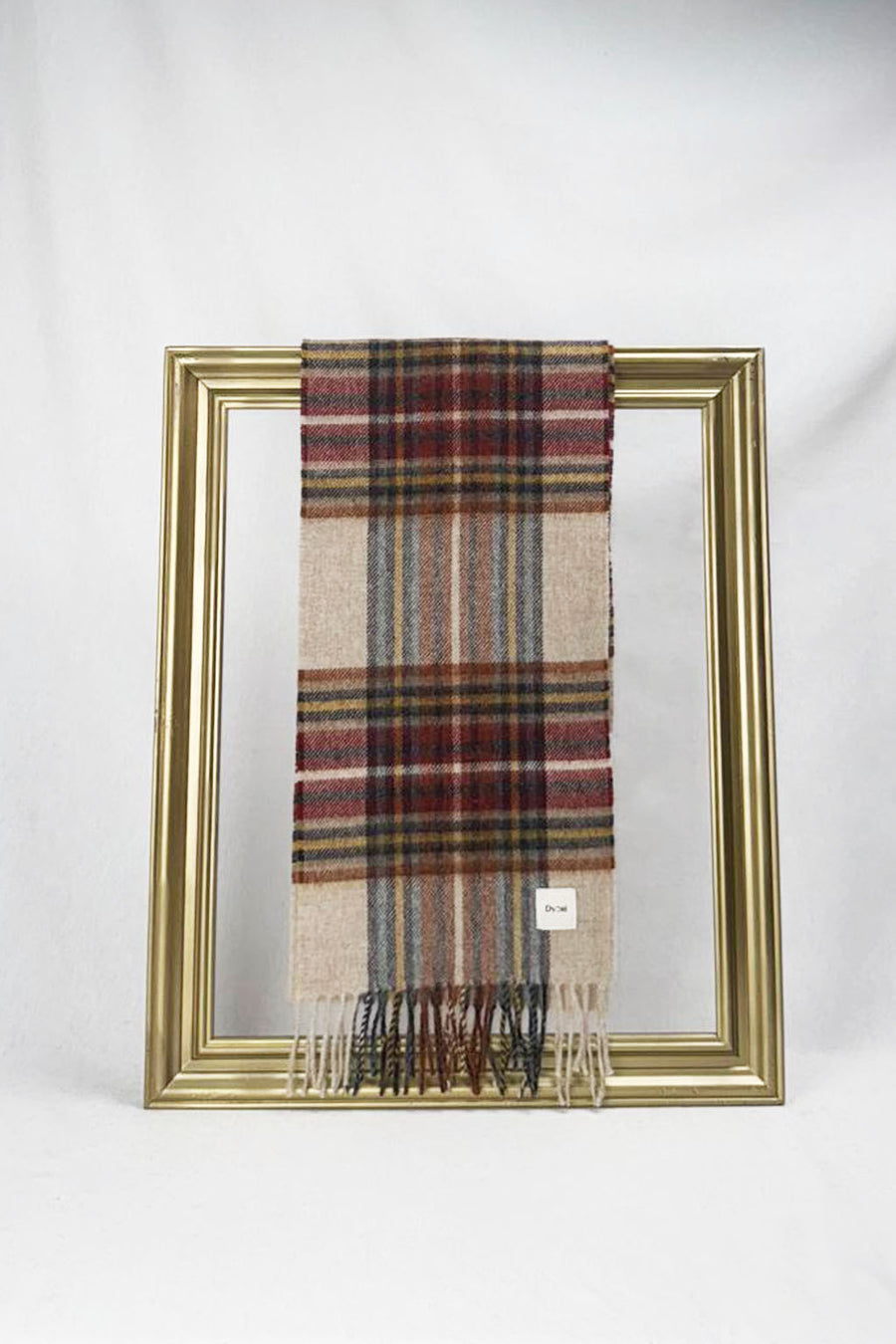 A beautifully designed beige tartan wool scarf featuring red, blue, and yellow checkered patterns is elegantly draped over a gold frame against a white background. The soft texture and timeless plaid design make it a perfect winter accessory and a thoughtful gift for her. Available with fast delivery across Malta.