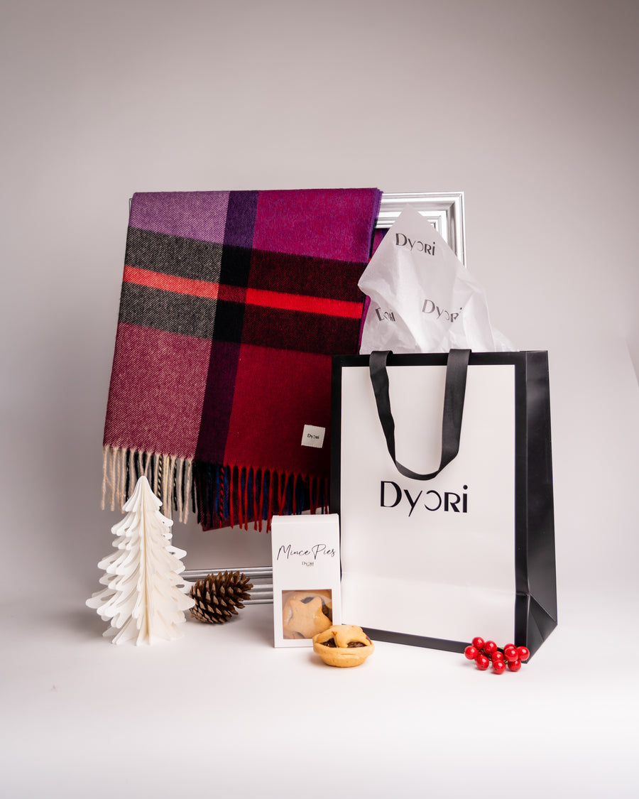 A rich burgundy and purple plaid wool scarf by Dyori arranged in a festive holiday scene with mince pies and Dyori’s premium gift bag – a perfect holiday present.