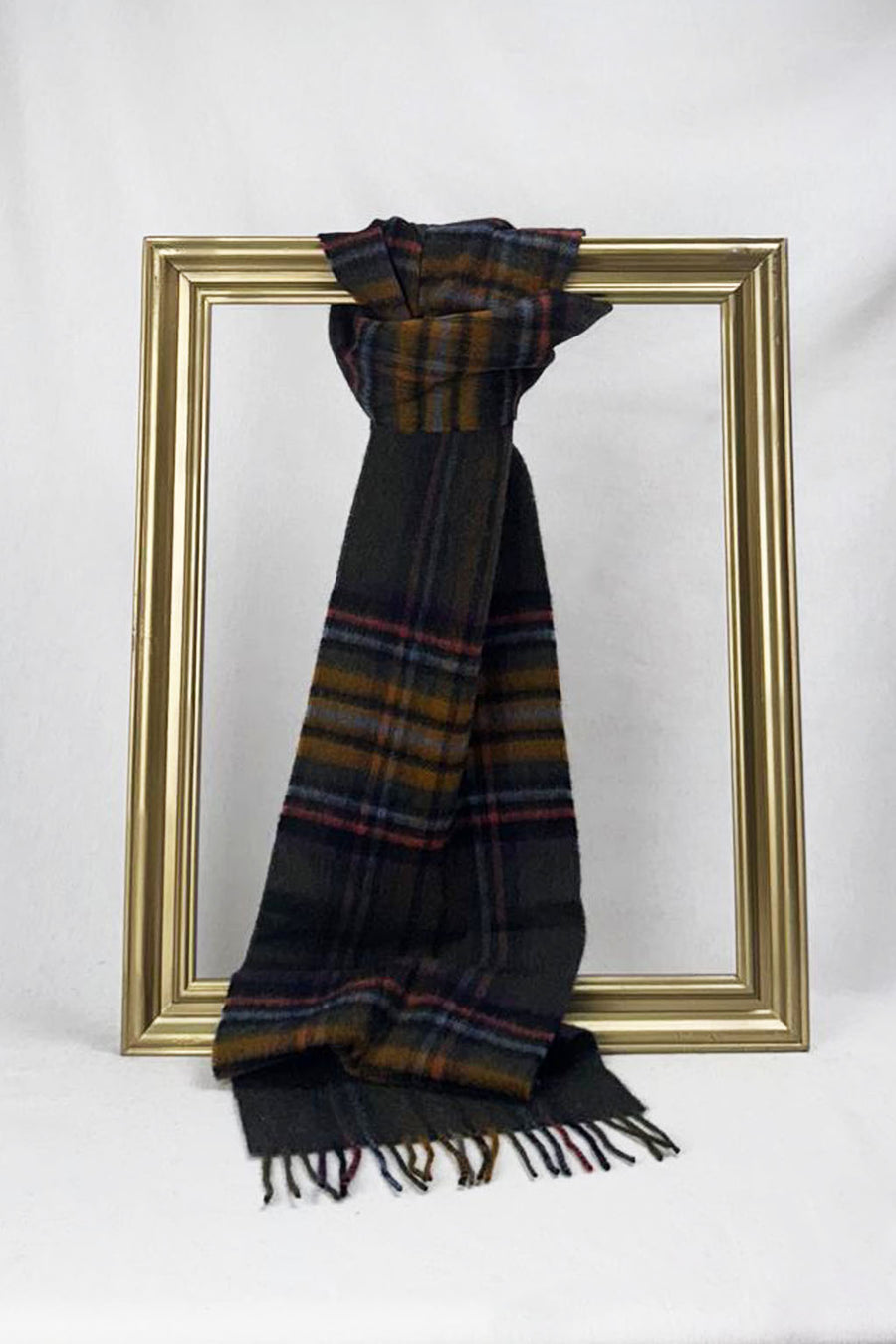 A luxurious wool scarf in a dark plaid pattern combining charcoal, mustard, and burgundy hues is elegantly looped through a gold frame. Displayed on a white background, it highlights timeless craftsmanship and warmth — an ideal cozy fashion gift for her with convenient delivery across Malta.