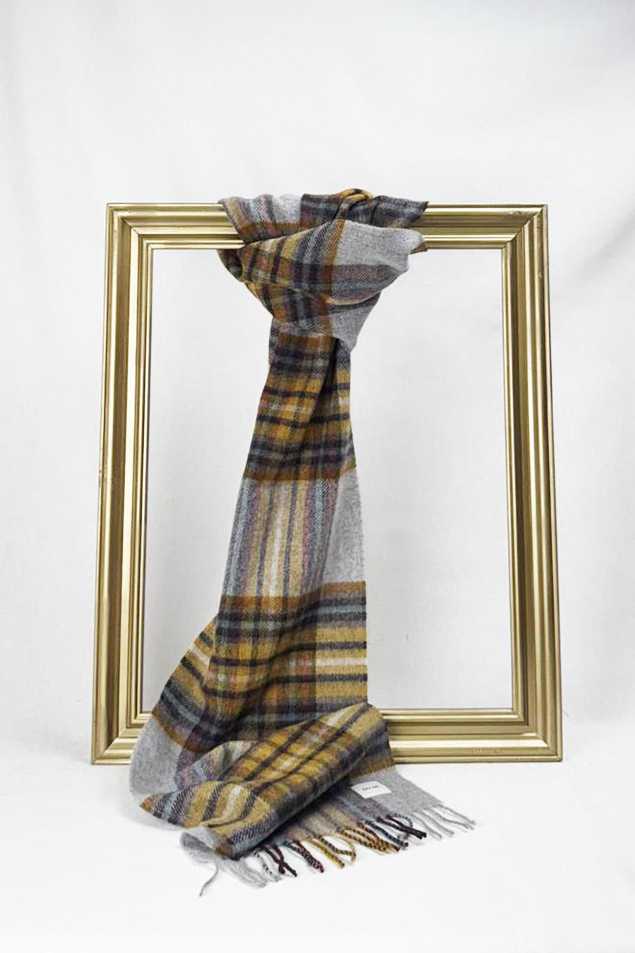 A beautifully displayed grey plaid wool scarf with warm mustard and burgundy checks hangs neatly over a gold frame against a plain white backdrop. The scarf’s soft weave and classic design highlight comfort and elegance, ideal as a cozy fashion gift for her with delivery across Malta.