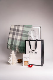 A luxurious green and grey plaid wool scarf by Dyori, styled in an elegant Christmas setup with a Dyori gift bag, pinecone, and mince pies – perfect for festive gifting.