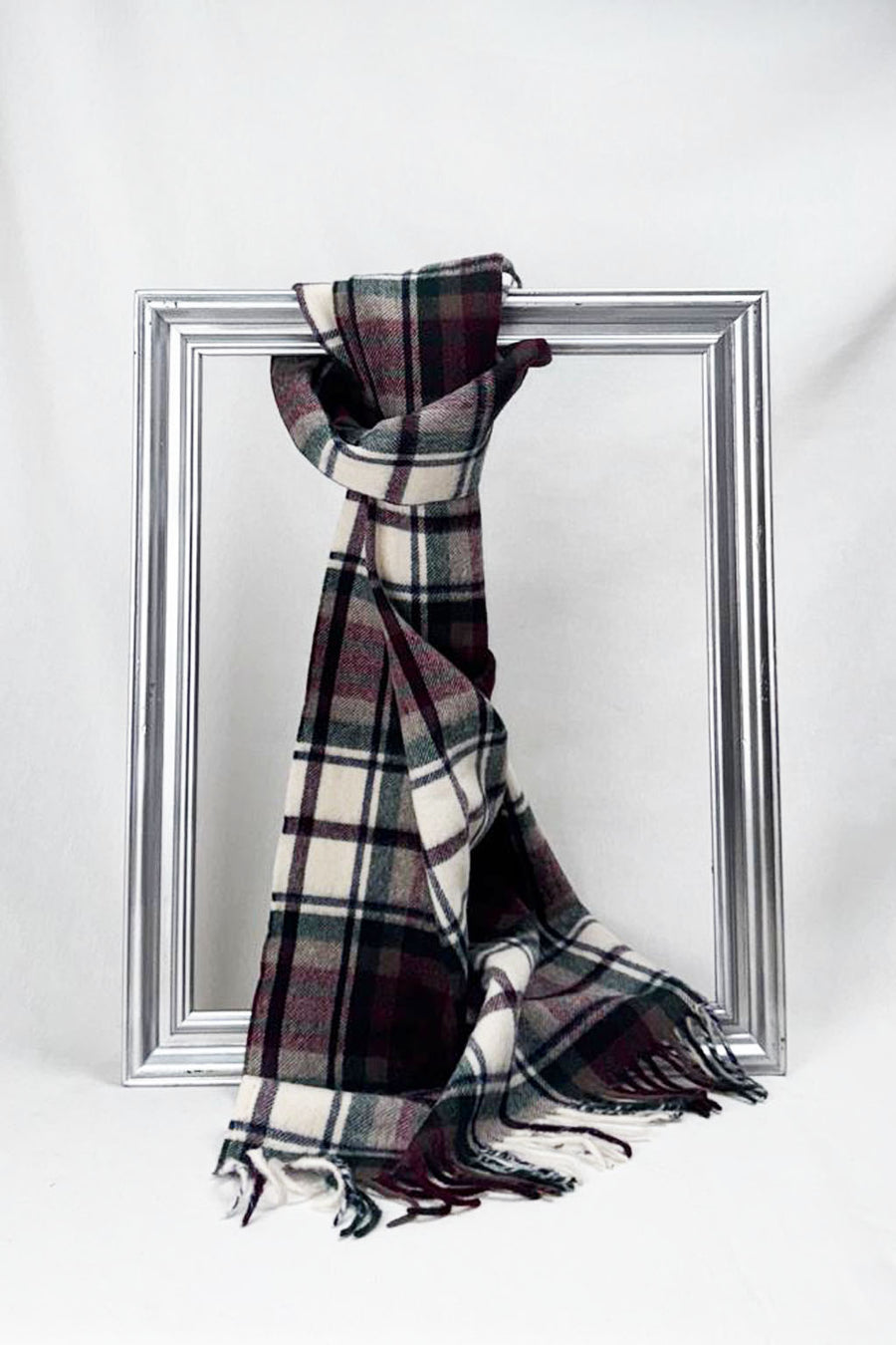 Luxurious merino wool scarf in a soft cream, burgundy, and forest green check pattern, beautifully draped over a silver frame. Warm, elegant, and perfect as a unisex winter gift. Available for delivery in Malta.