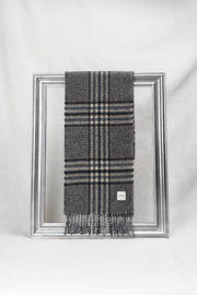 A sophisticated dark grey plaid wool scarf featuring beige and navy checkered patterns is neatly draped over a silver frame against a clean white background. The scarf’s refined design and soft texture showcase timeless winter fashion — a warm and elegant gift for him, available with delivery across Malta.