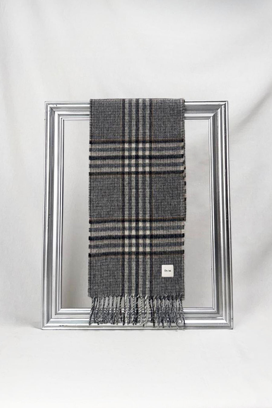 A sophisticated dark grey plaid wool scarf featuring beige and navy checkered patterns is neatly draped over a silver frame against a clean white background. The scarf’s refined design and soft texture showcase timeless winter fashion — a warm and elegant gift for him, available with delivery across Malta.