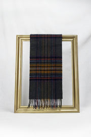 A premium dark tartan wool scarf featuring deep tones of charcoal, mustard, burgundy, and navy is neatly draped over a gold picture frame against a plain white background. The scarf’s classic plaid design and soft texture make it a stylish winter essential and a thoughtful gift for her, available with delivery across Malta.