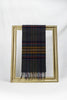 A premium dark tartan wool scarf featuring deep tones of charcoal, mustard, burgundy, and navy is neatly draped over a gold picture frame against a plain white background. The scarf’s classic plaid design and soft texture make it a stylish winter essential and a thoughtful gift for her, available with delivery across Malta.