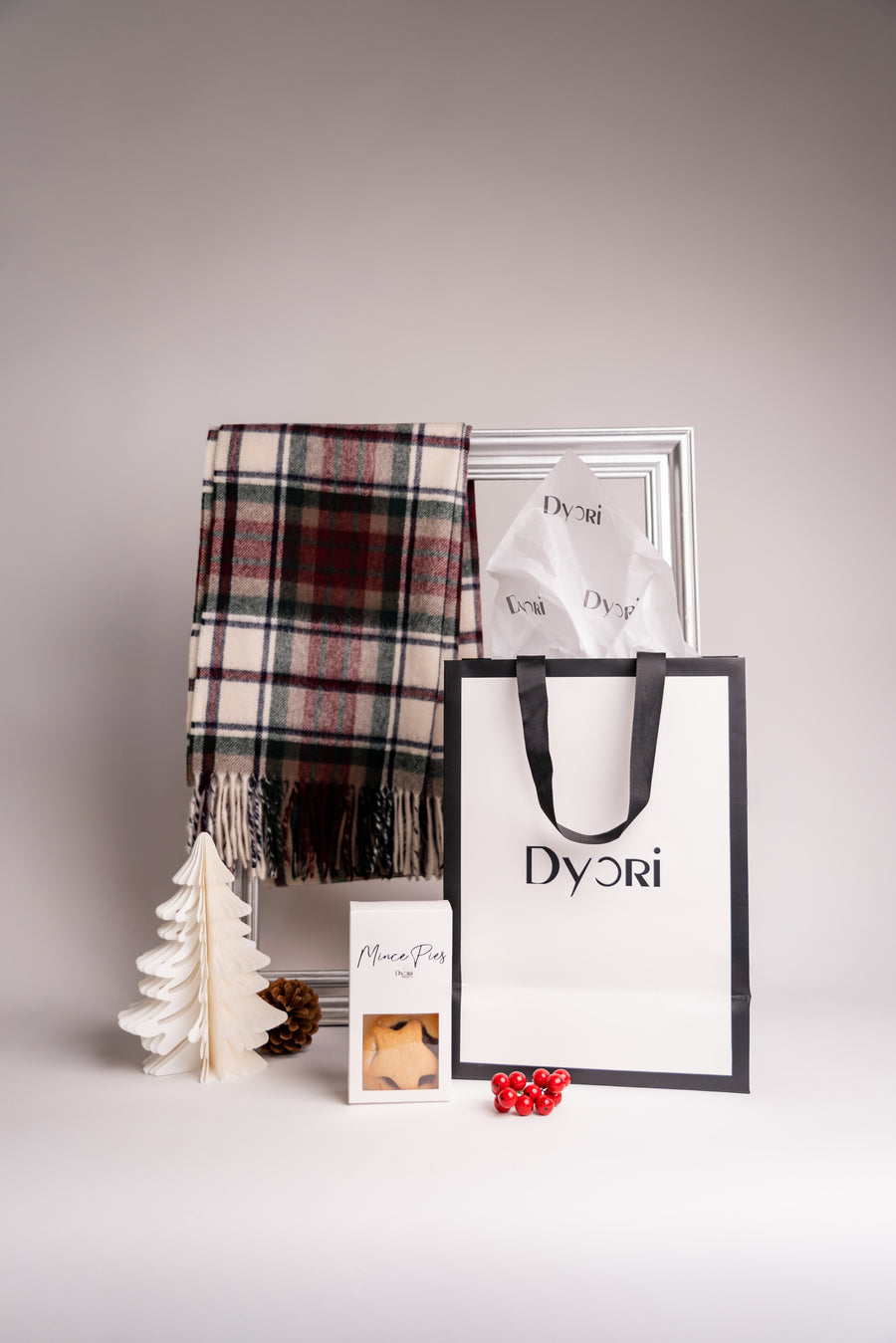 Elegant ivory and red merino wool check scarf from Dyori, styled in a warm holiday setup with mince pies, pinecones, and festive details — perfect for luxurious winter gifting.