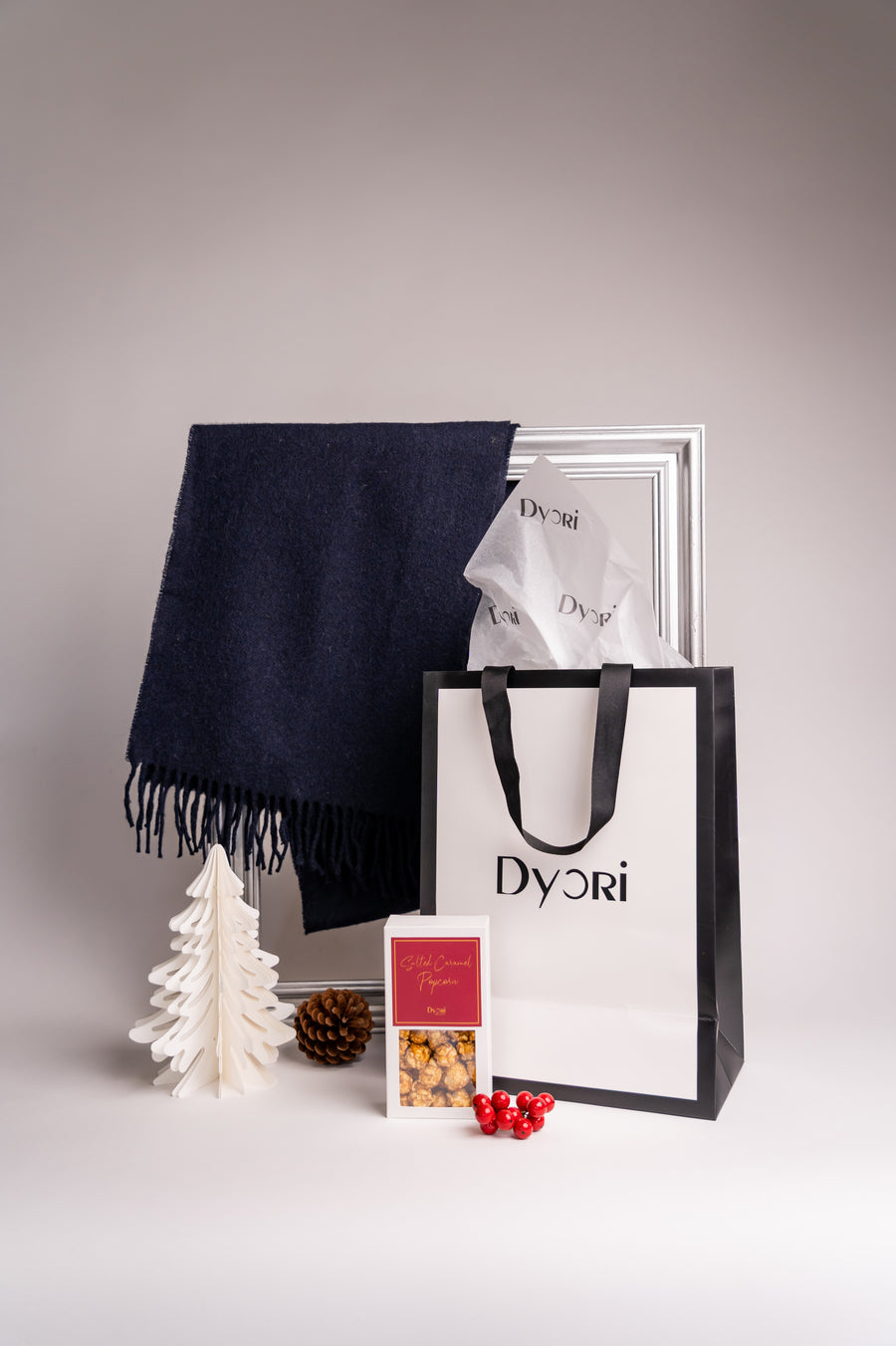 A luxurious solid navy blue merino wool scarf draped beside a Dyori shopping bag and minimal winter-themed decorations. The setup emphasizes refined simplicity and the softness of pure merino wool — a thoughtful gift choice.