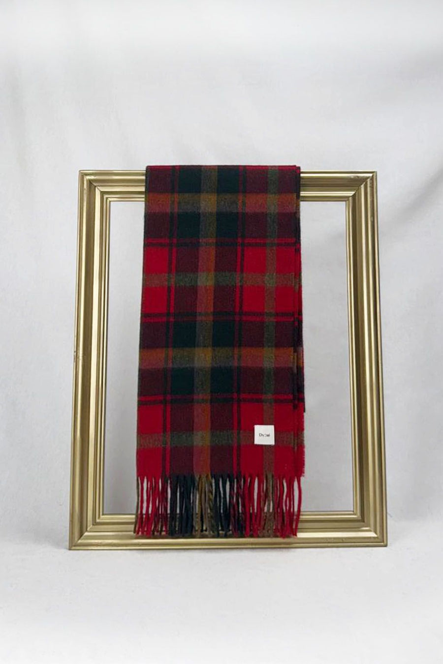 A classic red and green tartan scarf neatly folded on a gold frame, showcasing its rich Christmas colors and soft woven texture. A perfect gift for teachers — elegant, cozy, and beautifully packaged with delivery available across Malta.