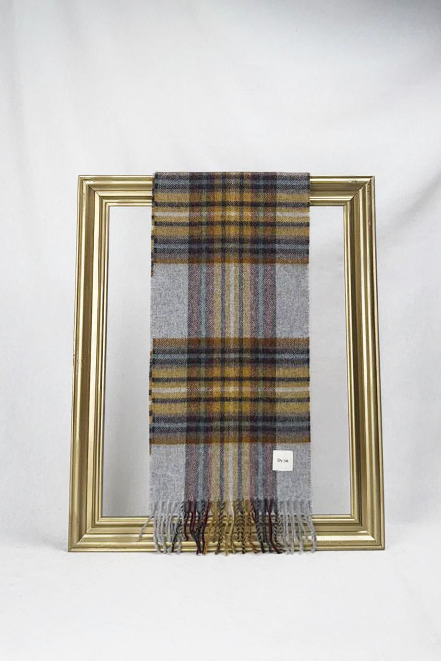 A luxurious grey tartan wool scarf featuring mustard, burgundy, and soft lavender stripes is gracefully looped through a gold picture frame. The rich plaid texture and soft fabric create a refined winter look, making it a stylish and thoughtful gift for her. Available with delivery across Malta.