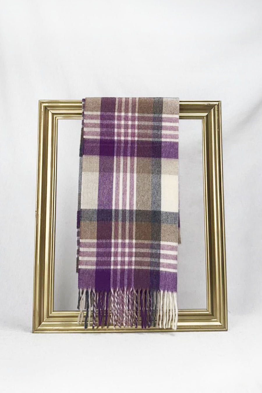 A luxurious plaid wool scarf featuring shades of purple, beige, grey, and cream is elegantly draped through a gold picture frame against a white background. This stylish winter accessory highlights warmth and sophistication, making it an ideal gift for her. Available with fast delivery across Malta.