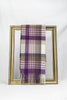 A luxurious plaid wool scarf featuring shades of purple, beige, grey, and cream is elegantly draped through a gold picture frame against a white background. This stylish winter accessory highlights warmth and sophistication, making it an ideal gift for her. Available with fast delivery across Malta.