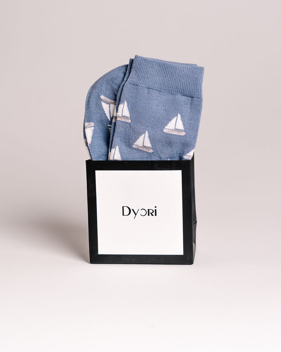 Blue socks with sailboat pattern in a black box with 'Dyori' branding on a light gray background