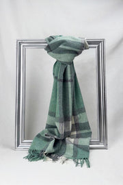 Luxurious merino wool scarf in a soothing green and grey check pattern, elegantly draped over a silver frame. Crafted for warmth and style, this premium unisex scarf makes a perfect winter gift for him or for her. Available for delivery in Malta.