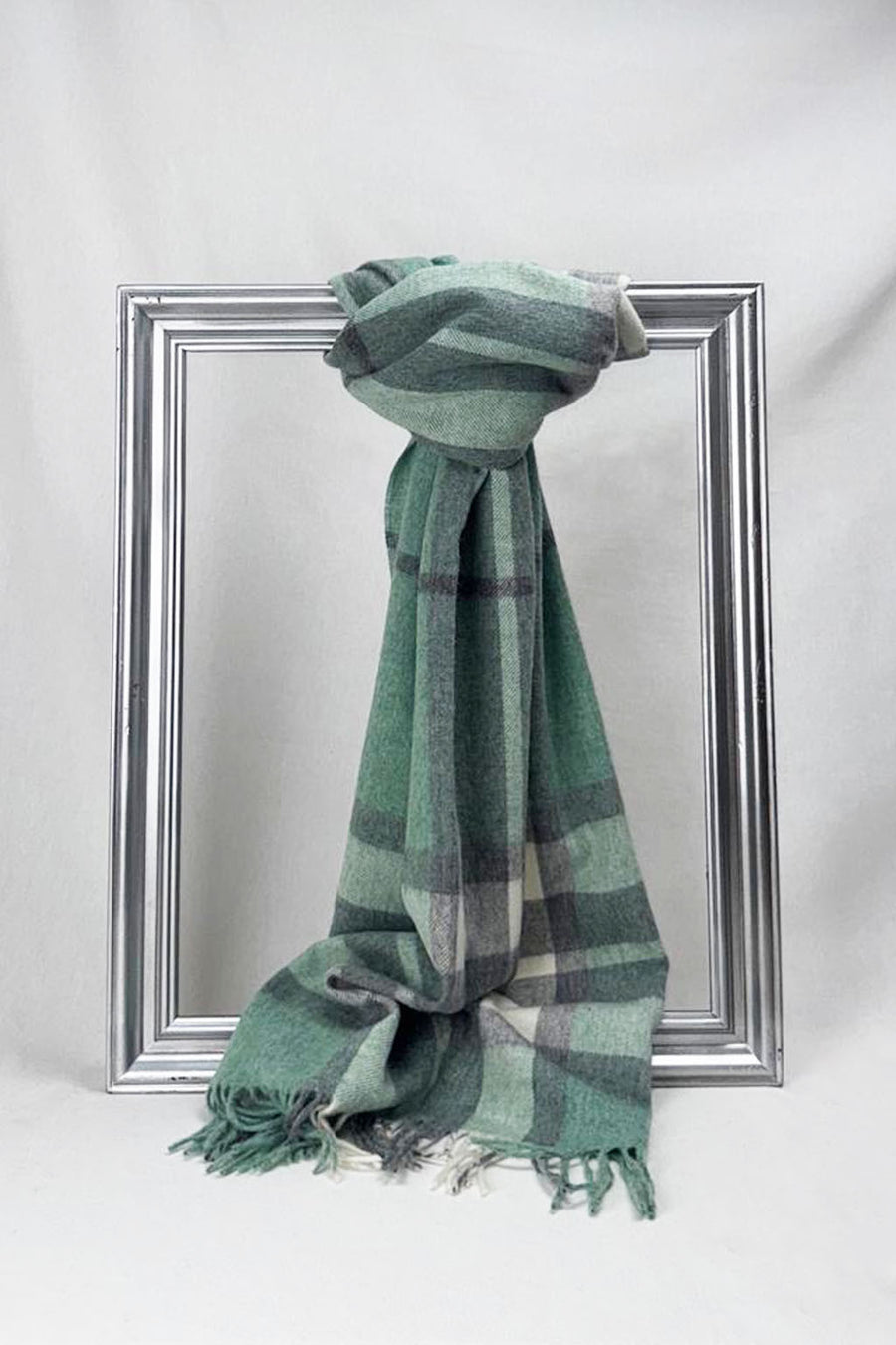 Luxurious merino wool scarf in a soothing green and grey check pattern, elegantly draped over a silver frame. Crafted for warmth and style, this premium unisex scarf makes a perfect winter gift for him or for her. Available for delivery in Malta.