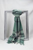 Luxurious merino wool scarf in a soothing green and grey check pattern, elegantly draped over a silver frame. Crafted for warmth and style, this premium unisex scarf makes a perfect winter gift for him or for her. Available for delivery in Malta.