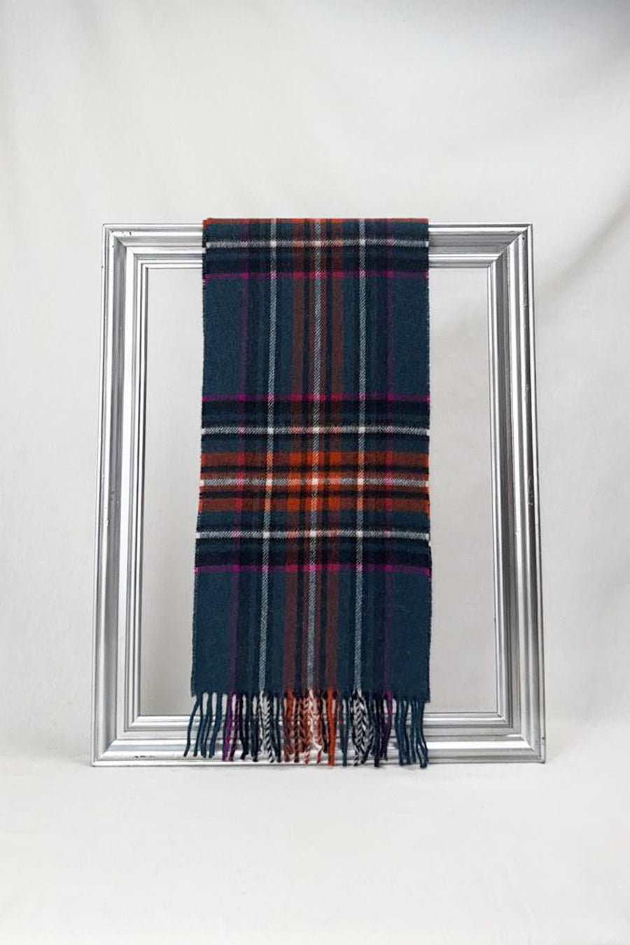 Soft merino wool scarf in a rich teal, rust, and magenta check pattern, elegantly draped over a silver frame. Cozy, stylish, and perfect as a unisex winter accessory. Delivered in Malta.