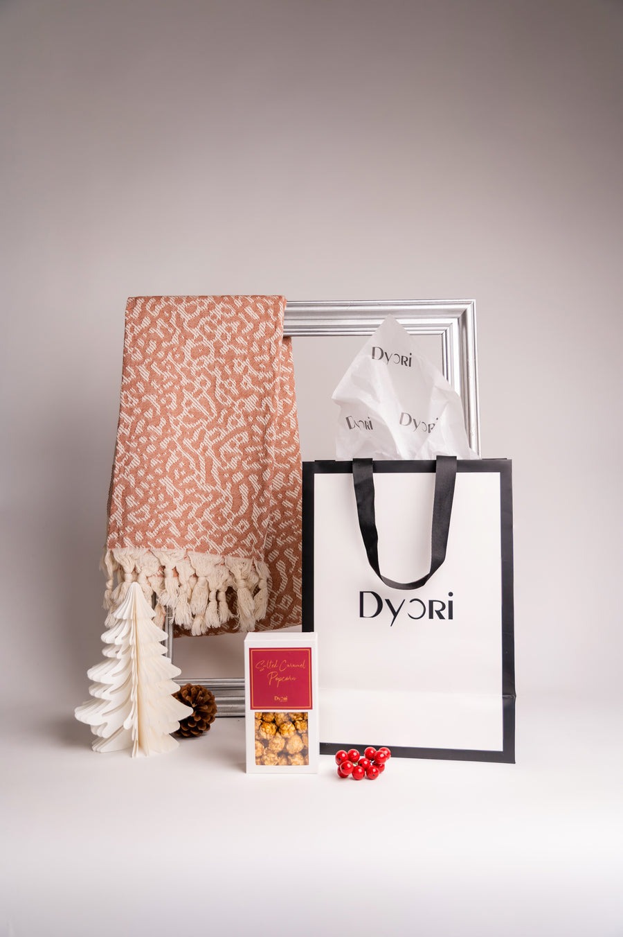 A soft terracotta-colored 100% cotton shawl made in Turkey, featuring a delicate jacquard weave with hand-knotted tassels, elegantly styled with a Dyori gift bag and festive treats.