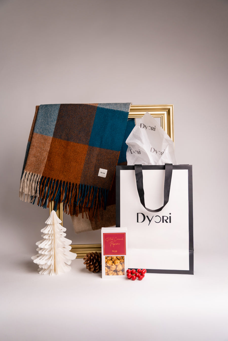 Festive gift set featuring a warm autumnal check wool shawl in rust, teal, and beige tones, with Dyori gift bag and salted caramel popcorn.