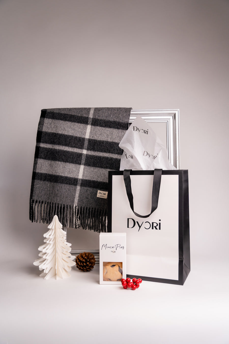 Festive gift set featuring a grey and black checked wool shawl, Dyori gift bag, and box of mince pies displayed with Christmas decor.