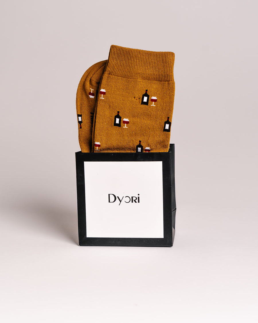 Mustard yellow socks with wine-themed design in a black box with 'Dyori' branding on a light gray background. Secret santa gifts 