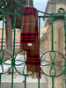 Elegant merino wool scarf in a rich brown and red check pattern with fringed edges, draped over a silver frame. A timeless unisex winter accessory, available in Malta.