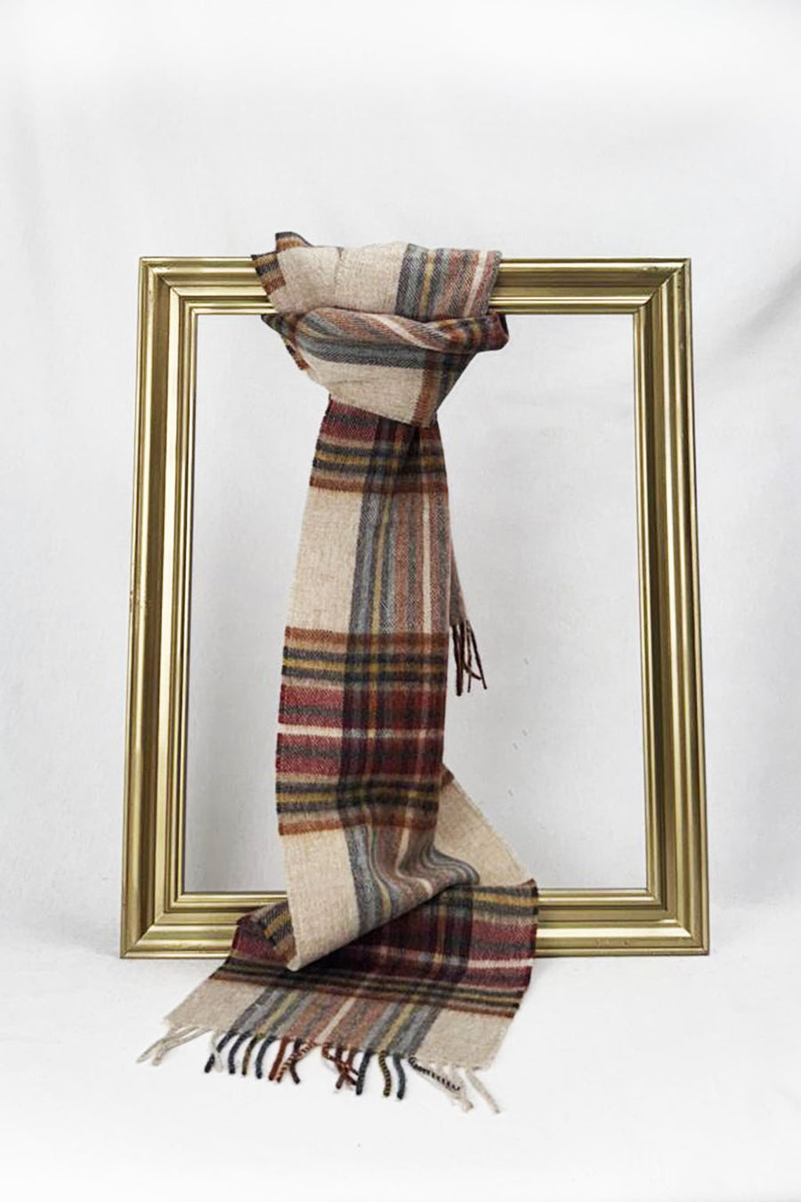 A luxurious beige plaid wool scarf with rich tones of red, blue, and mustard is gracefully looped through a gold picture frame. Set against a clean white backdrop, this elegant scarf showcases its fine weave and classic charm — a cozy and stylish gift for her with delivery available across Malta.