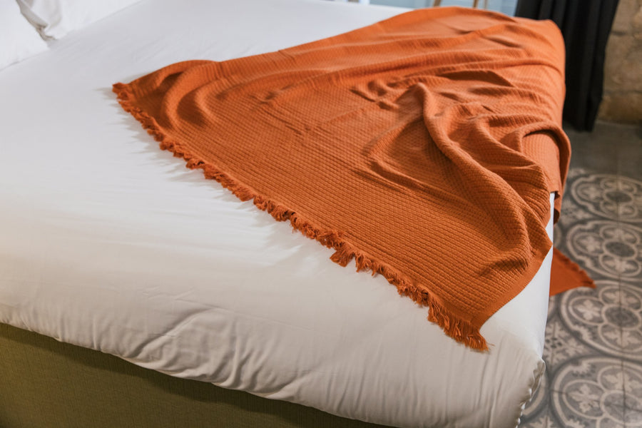 A luxurious Turkish cotton throw in a warm coral hue, featuring a soft waffle texture and fringed edges — perfect for adding a pop of colour and cozy comfort to any space